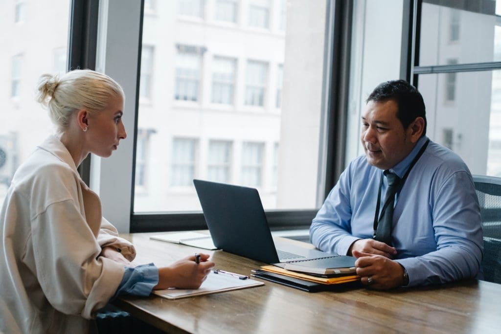 Woman sitting across from man with a laptop in a professional setting.